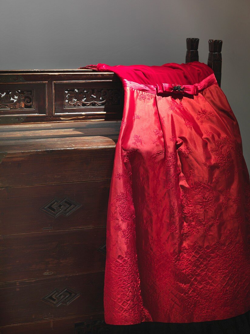 Elegantes rotes Abendkleid auf antiker Kommode liegend