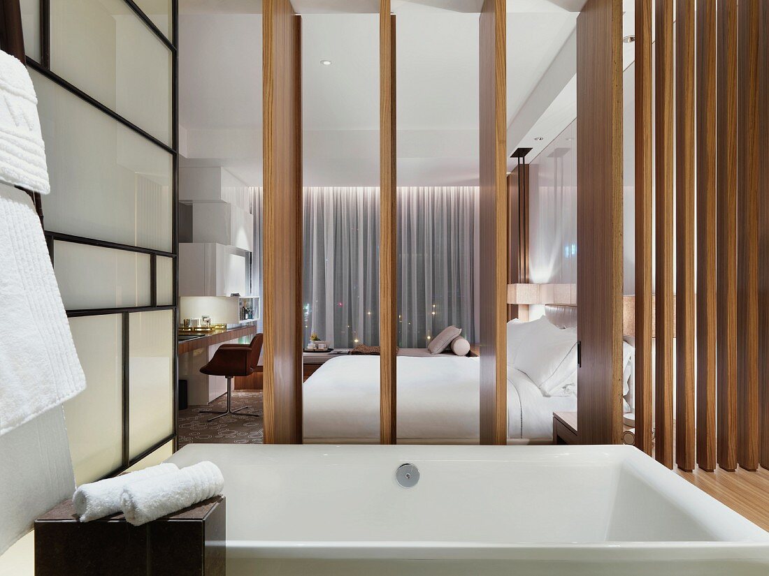 Quadratische Badewanne in Hotelbadezimmer mit geöffneter Holzschiebewand zum Schlafbereich