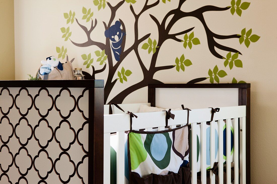 Babybett vor Wand mit aufgemaltem Baum in Kinderzimmer