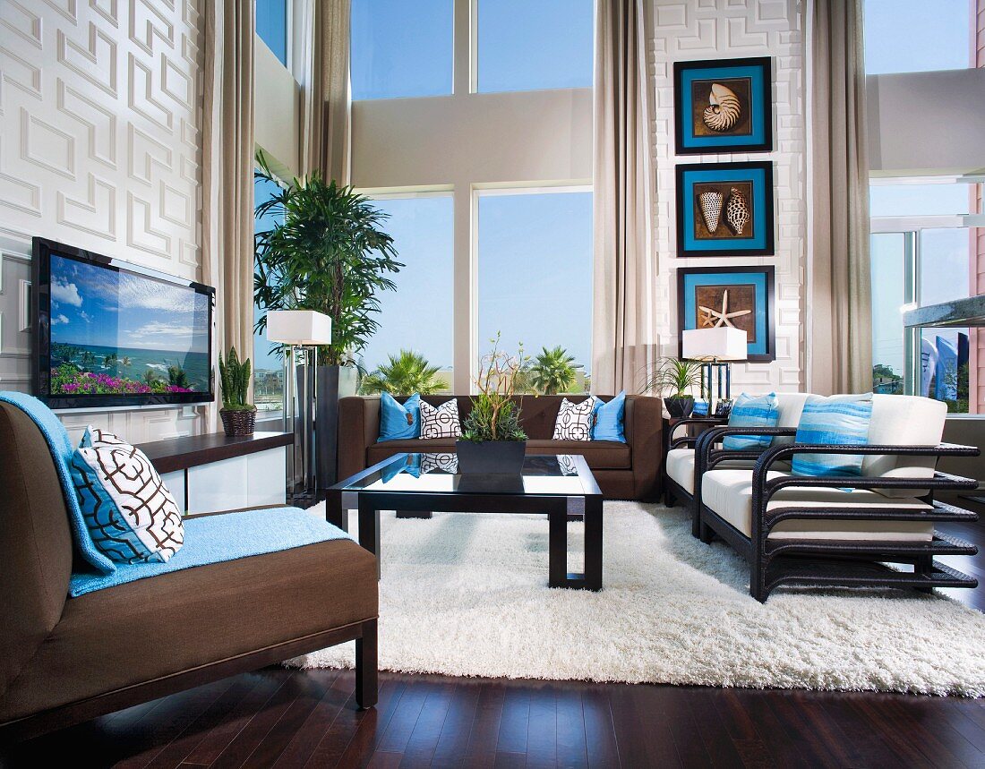 Modernes Wohnzimmer in Braun & Weiß mit blauen Farbakzenten, breiter Fensterfront und Sitzecke mit Flachbildschirmfernseher