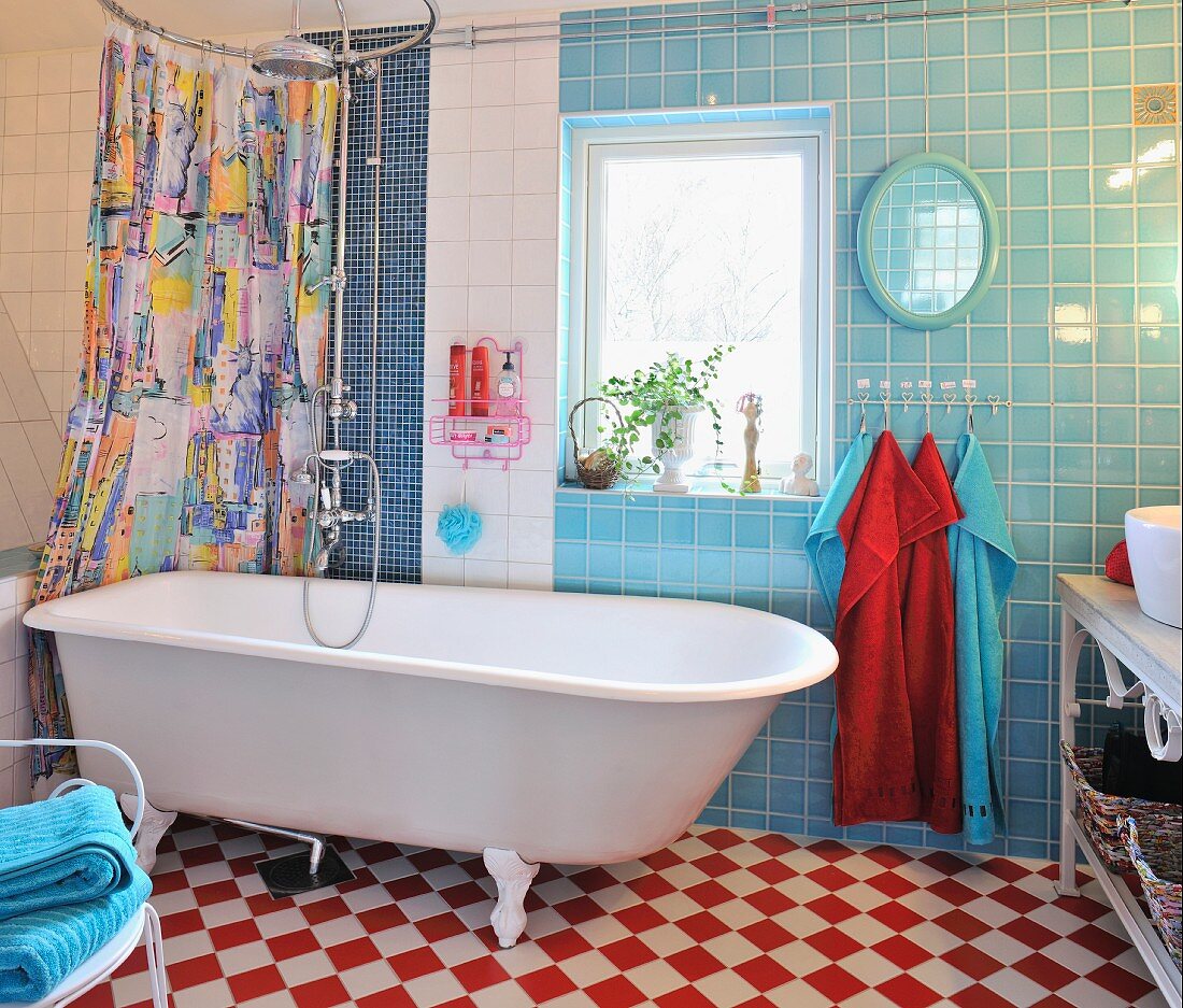 Colourful shower curtain behind retro bathtub, blue and white wall tiles and red and white chequered floor tiles