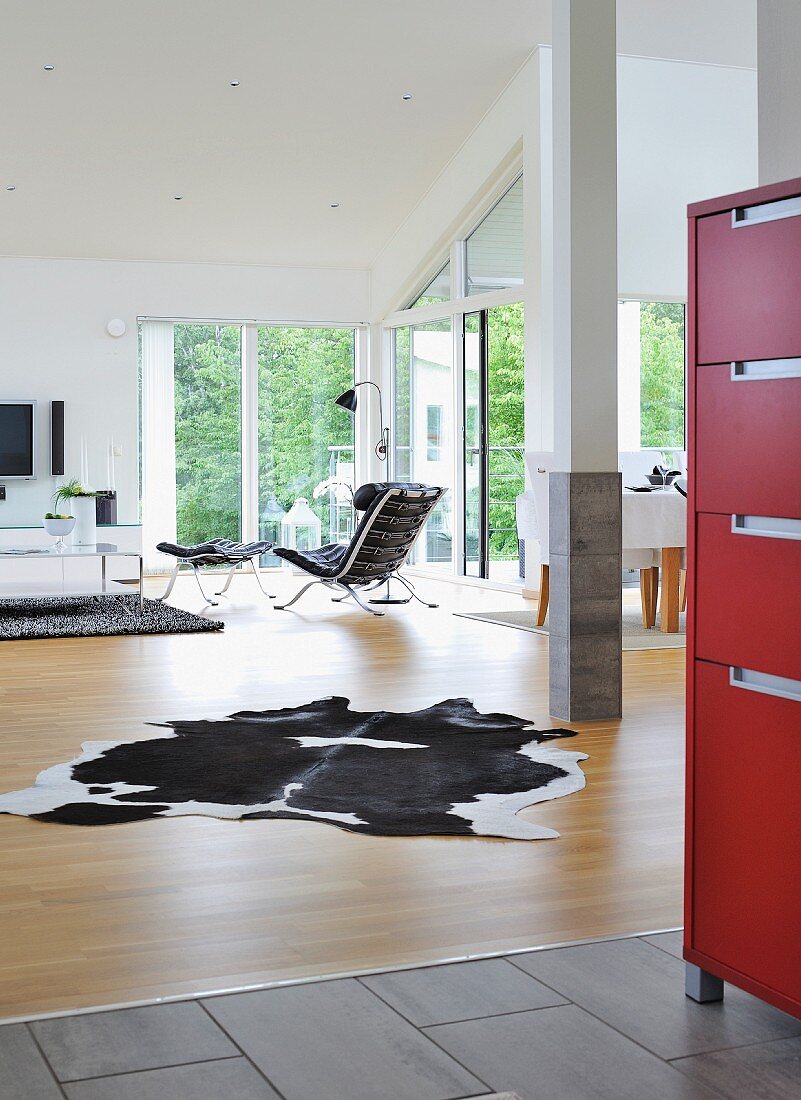 Blick in hellen, offenen Wohnraum mit Tierfellteppich, im Hintergrund Sessel mit passendem Fussschemel im Klassikerstil