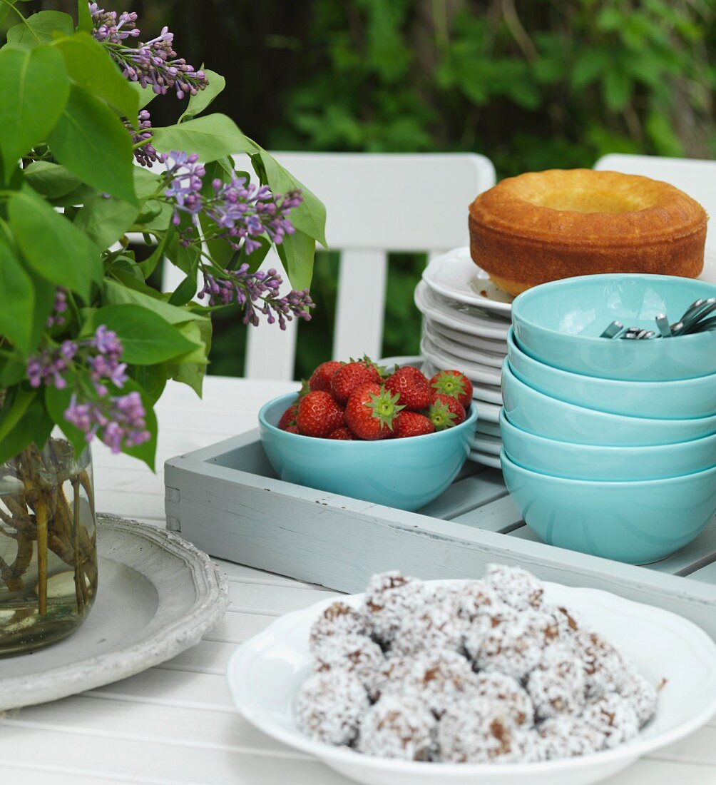 Schokokugeln auf weisser Schale, Tablett mit blauen Schalen, Erdbeeren und Kuchen auf Gartentisch