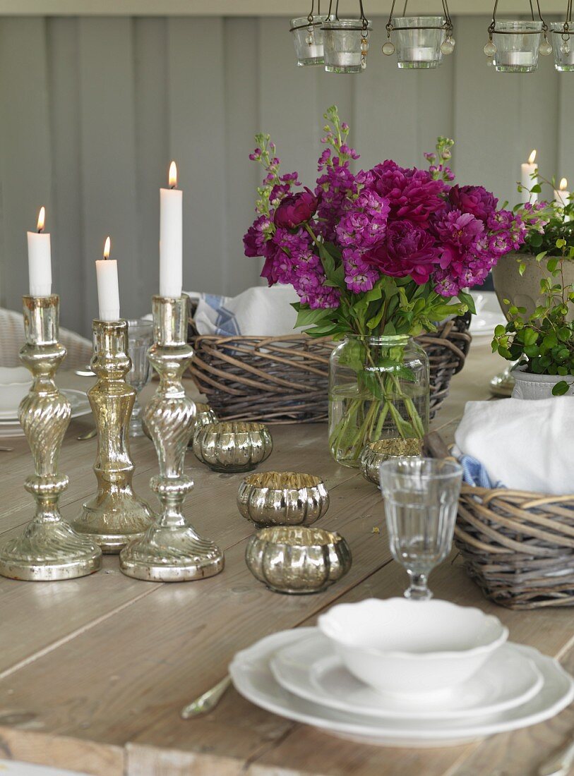 Lit candles in silver candlesticks on set table in rustic interior