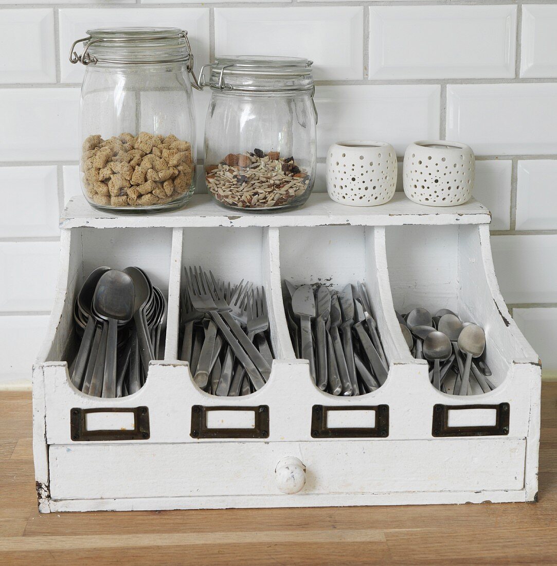 Storage jars and tealight holders on old, white-painted cutlery tray with drawer