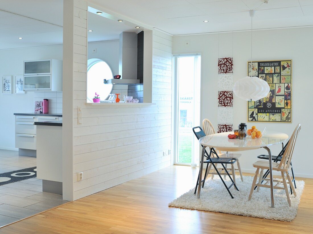 Heller Essplatz mit verschiedenen Stühlen auf Flokatiteppich und Wandscheibe mit Durchreiche zur Küche; Landhaus Flair
