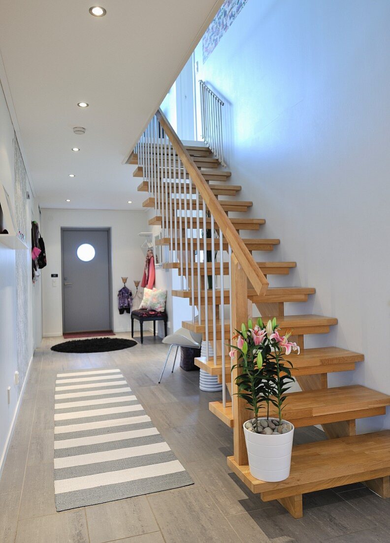 Zeitgenössischer Hauseingang mit Garderobe, Einbauschränken und heller Holztreppe, auf Fliesenboden grau-weiß gestreifter Teppichläufer