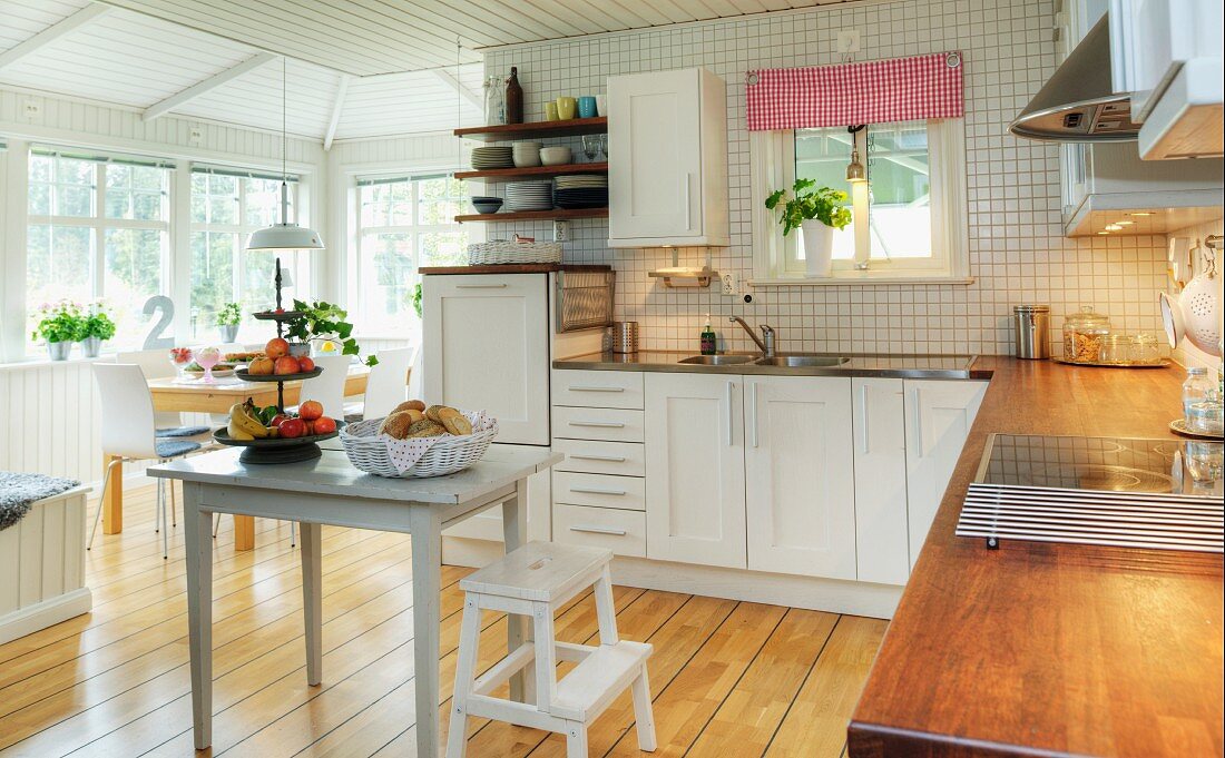 Geräumige, schwedische Wohnküche mit weißem Küchenschrank; Essplatz in wintergartenähnlichem Anbau