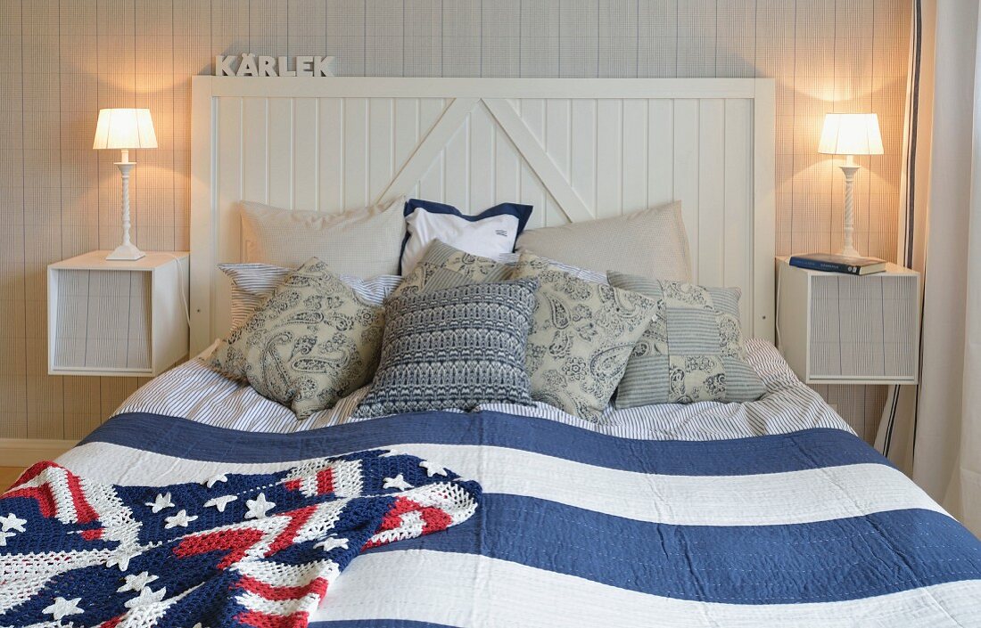 Doppelbett mit Holzkopfteil, blau-weiss gestreiftem Überwurf und gehäkelter 'Stars and Strips' Decke