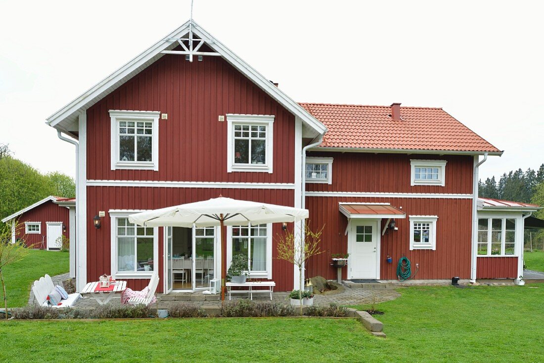 Falu red and white Swedish wooden house with terrace situated in lush, green landscape