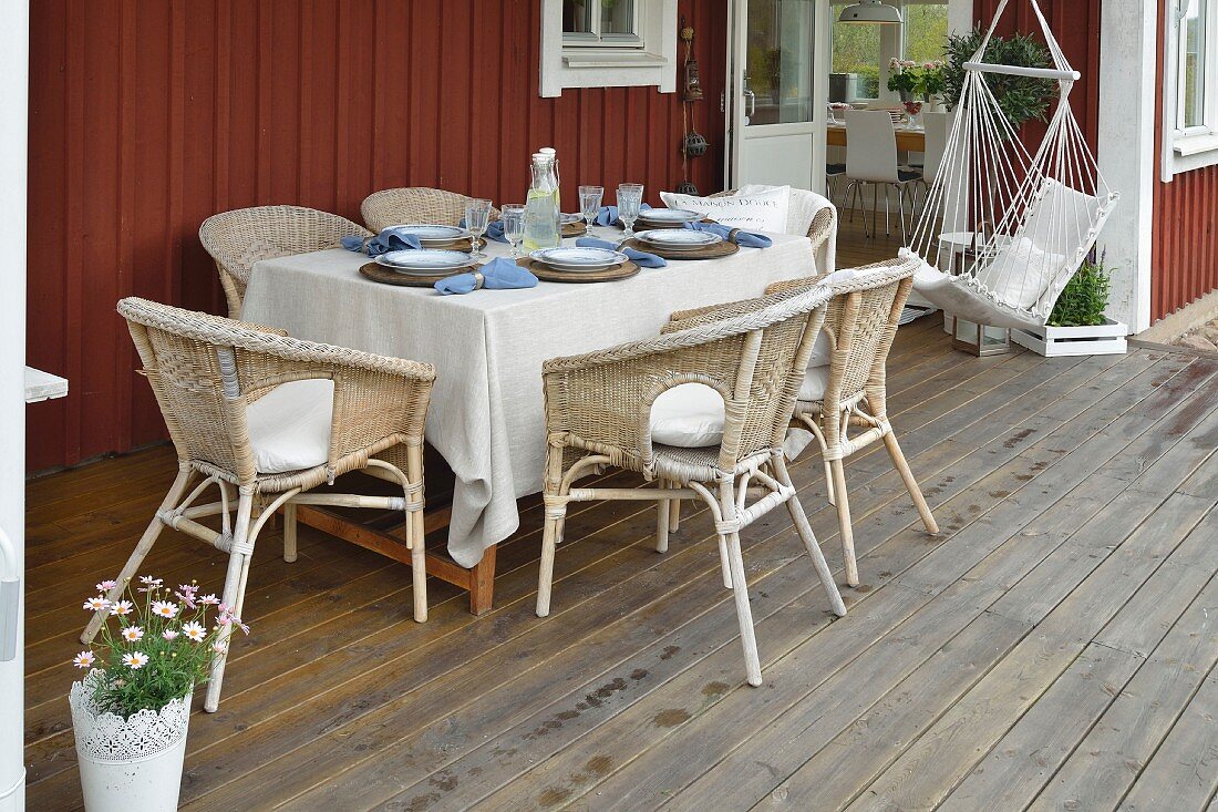 Gedeckter Tisch mit Rattansesseln und Hängesitz auf der Veranda eines Schwedenhauses