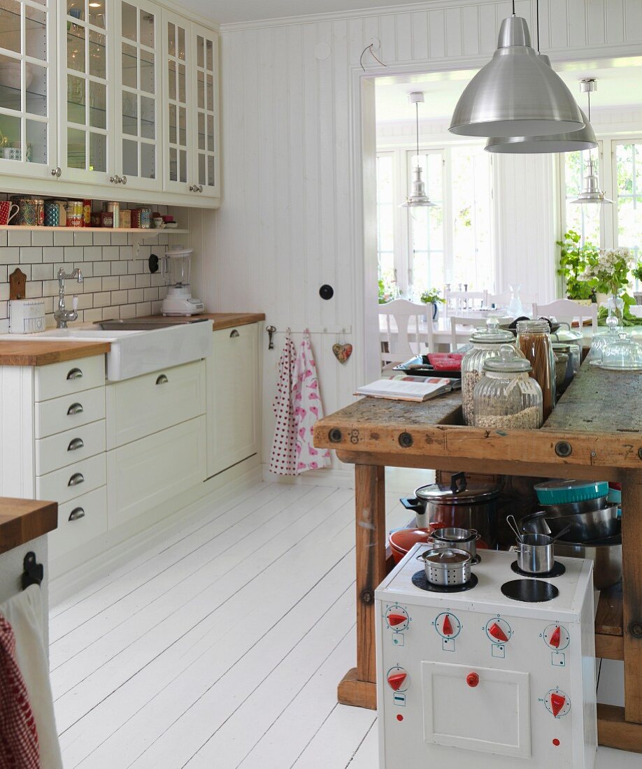 Toy cooker in front of old workbench converted into kitchen counter in Scandinavian kitchen-dining room with white wooden floor