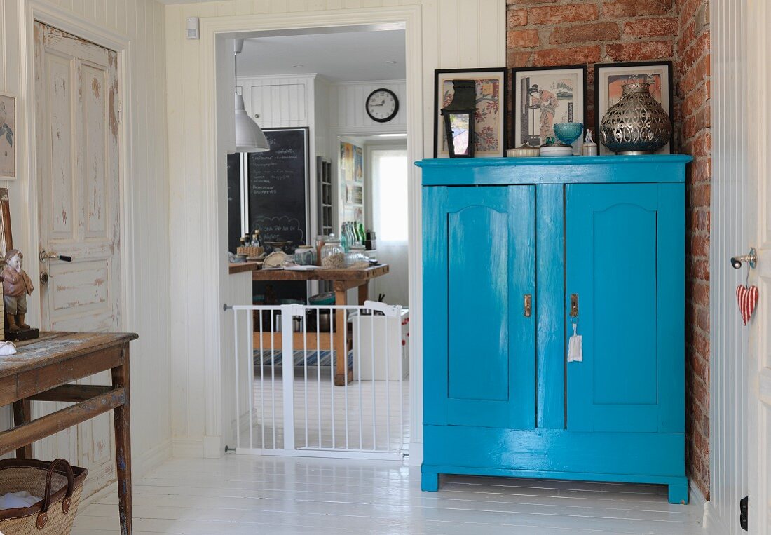 Blue-painted farmhouse cupboard against brick wall next to baby gate in kitchen doorway