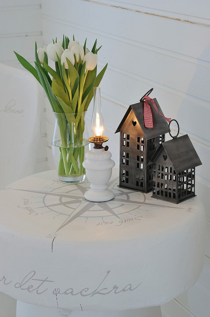 Tulpenstrauss, Petroleumlampe und Miniaturhäuser, auf weiss lackiertem Baumstammtisch mit Deko-Beschriftung