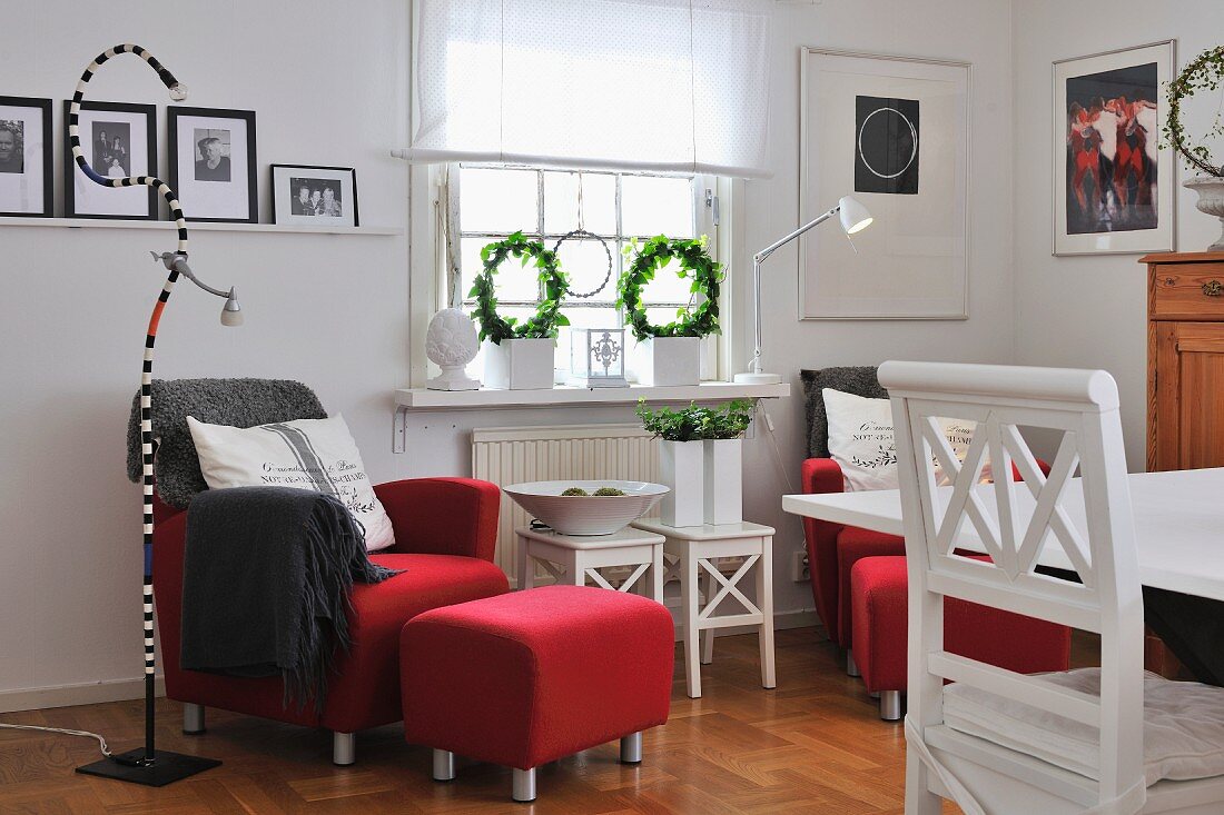 Wohnraum im skandinavischen Landhausstil mit roten Sesseln, weiss gestrichenen Holzmöbeln und Schlangen-Stehleuchte
