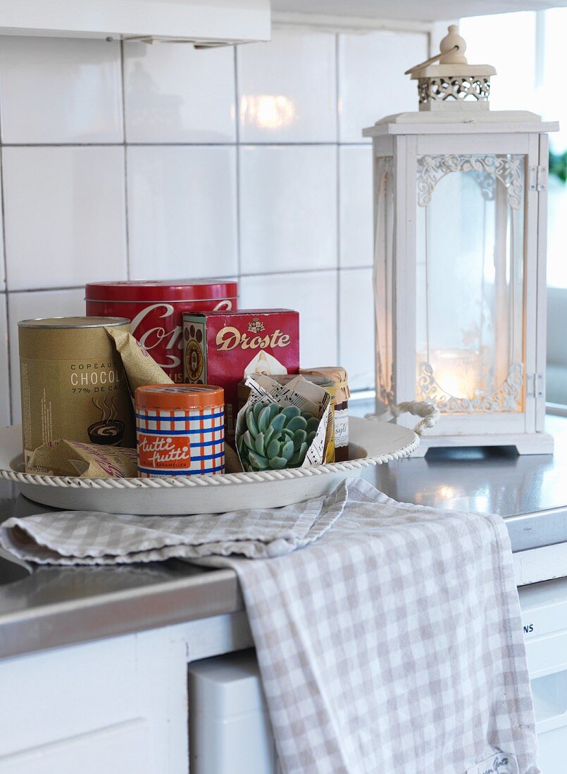 Schale mit Aufbewahrungsdosen, davor Geschirrtuch und Laterne im Vintage Stil, weiss lackiert auf Küchenzeile