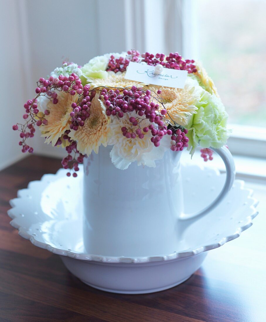 Weisser Keramikkrug mit Blumen und Beerenzweigen dekoriert, auf Schale