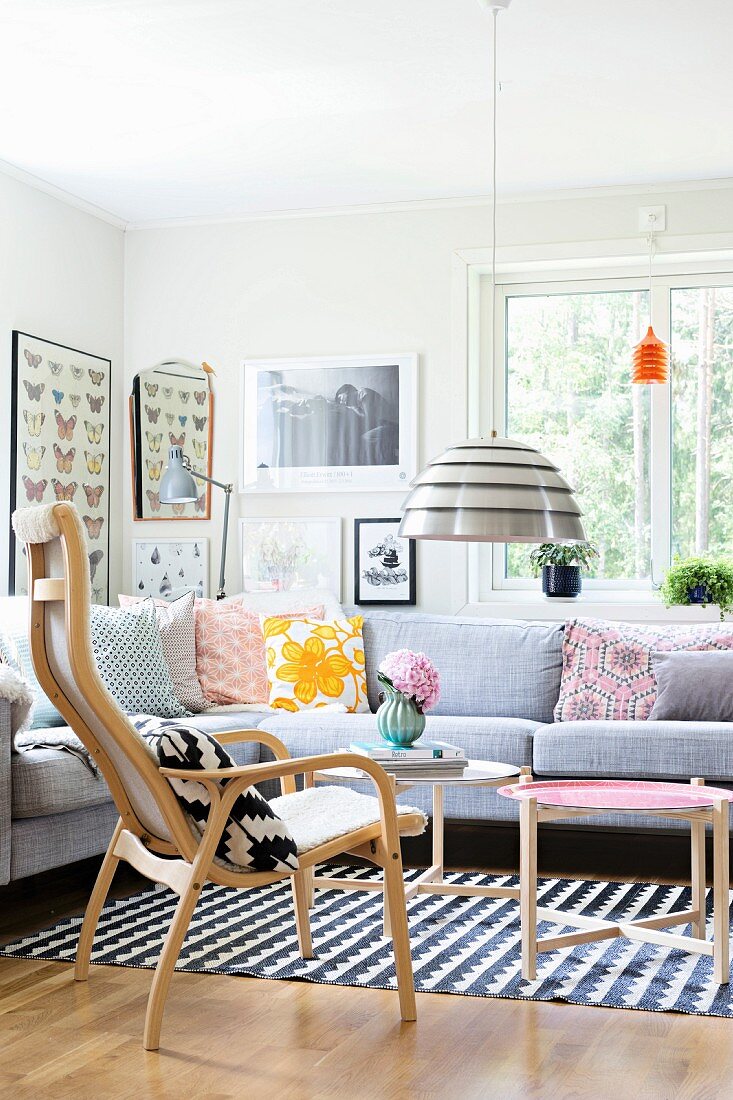 Sitzgruppe mit Retro-Kissen auf Überecksofa und skandinavischen Holzmöbeln; Bildergalerie an Wand im Hintergrund