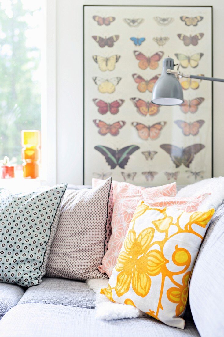 Retro-Kissen auf Überecksofa und Bild mit Schmetterlingsdarstellungen im Hintergrund