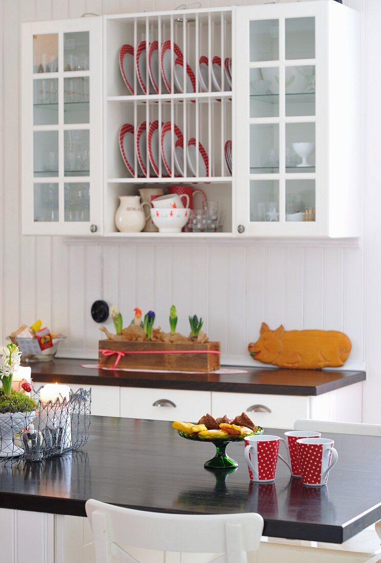 Blick von der Frühstückstheke mit rot-weissen Bechern auf Hängeschrank mit Tellerregal