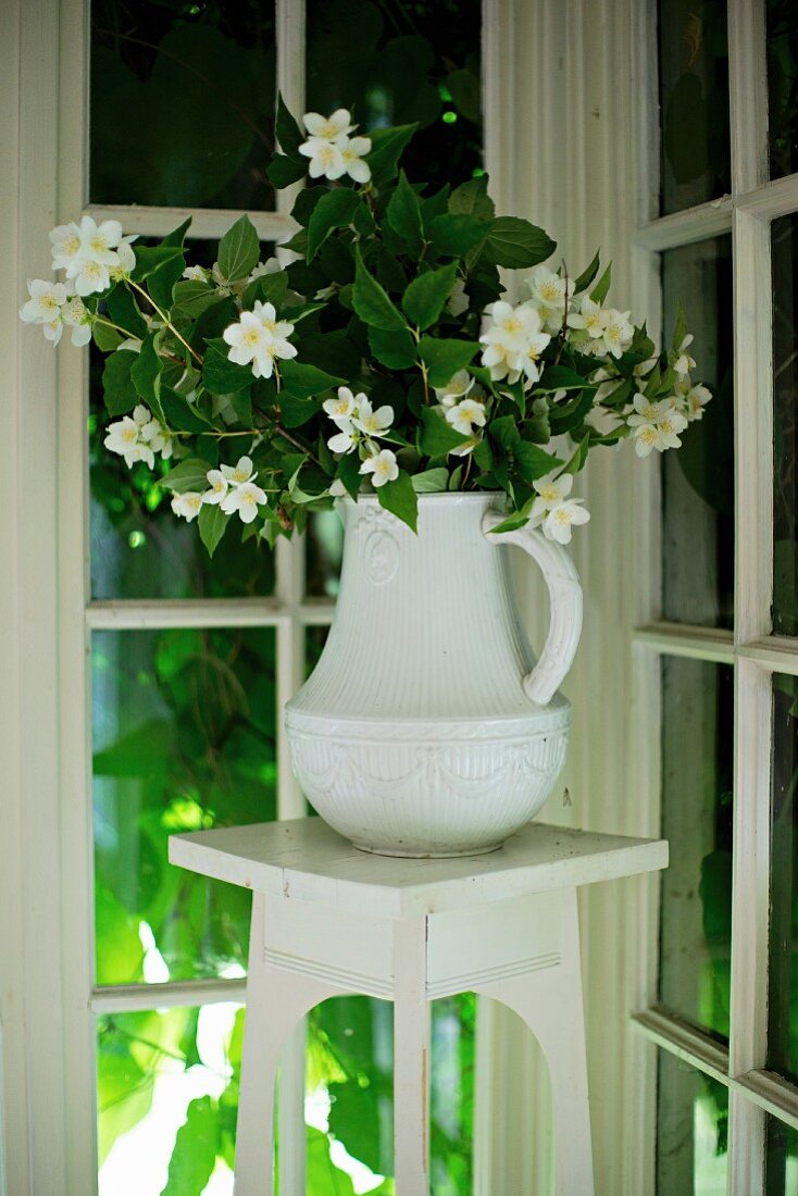 Weisser Porzellankrug mit Jasminblüten auf Blumenständer