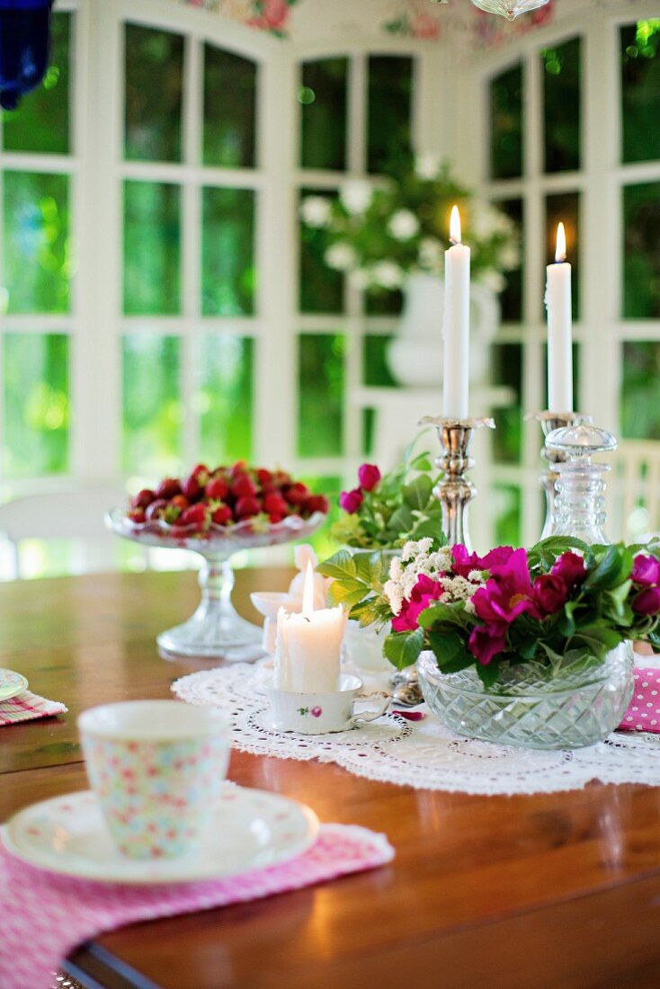 Gedeckter Tisch mit Blumenschale, Kerzen und frischen Erdbeeren