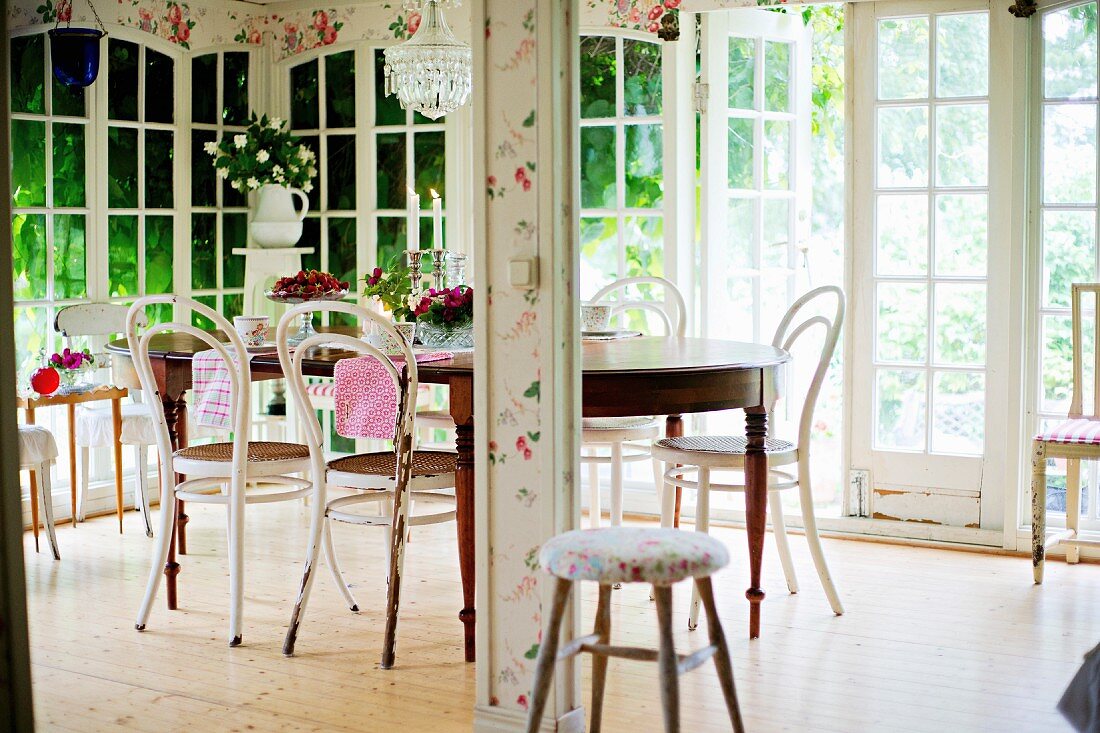 Thonetstühle mit weisser, abblätternder Farbe um antikem Holztisch im Wintergarten