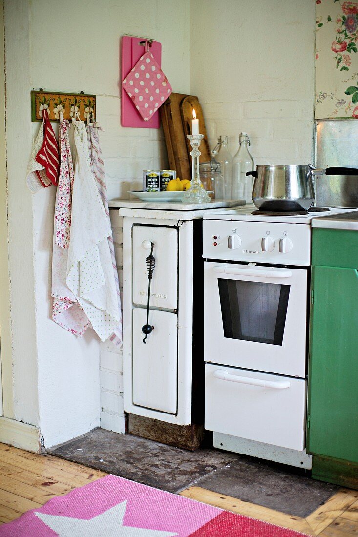 Solid-fuel stove, cooker and tea towels hanging from wall hooks in corner of kitchen