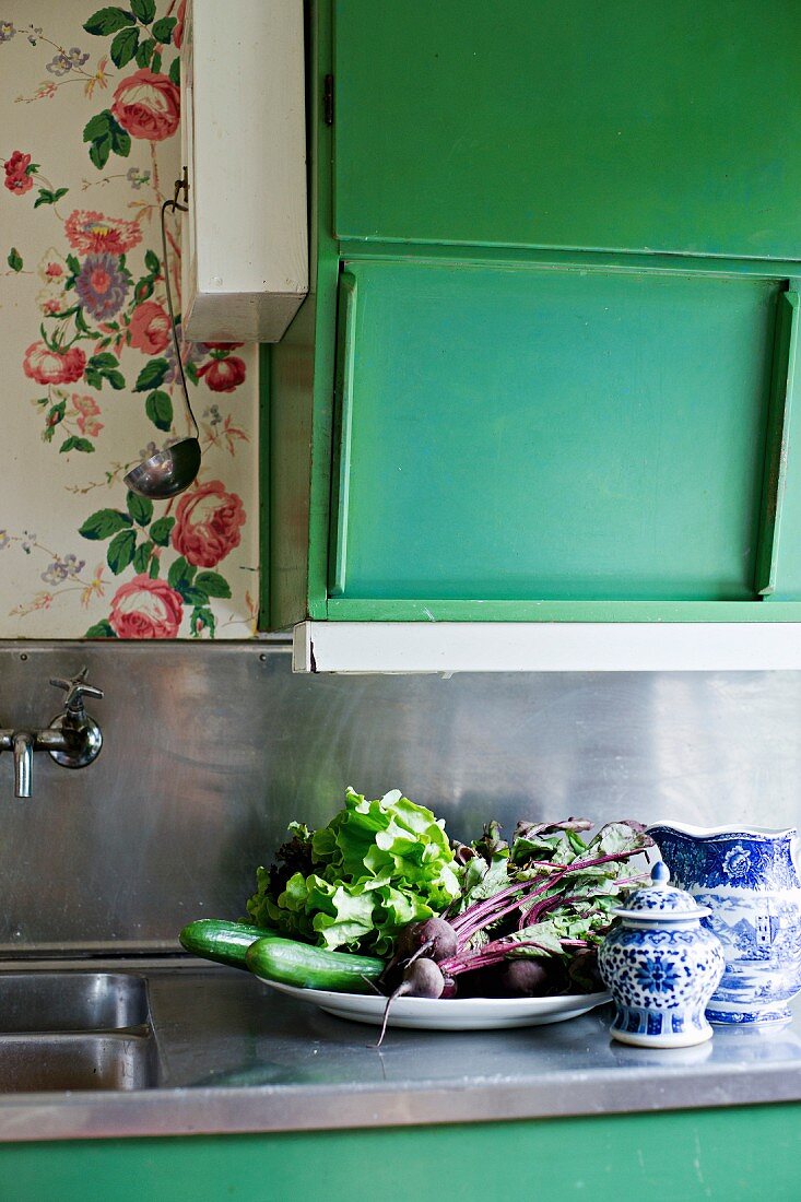 Geerntetes Gemüse auf Teller neben weiss-blauem Geschirr unter grünem Hängeschrank