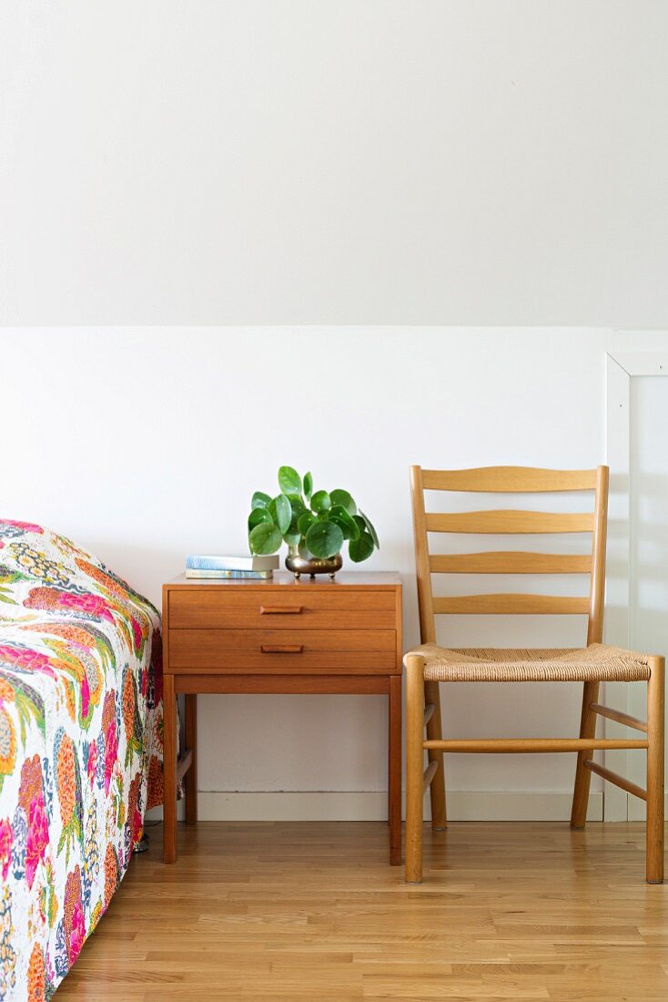 Nachttisch, heller Holzstuhl und Bett mit buntem Überwurf in Dachgeschossschlafzimmer
