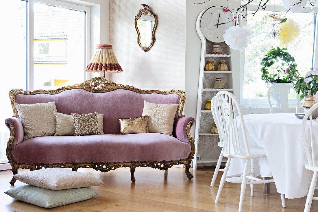 Sofa im Barockstil mit fliederfarbenem Samtbezug, Kissenstapel und Essplatz in Weiß