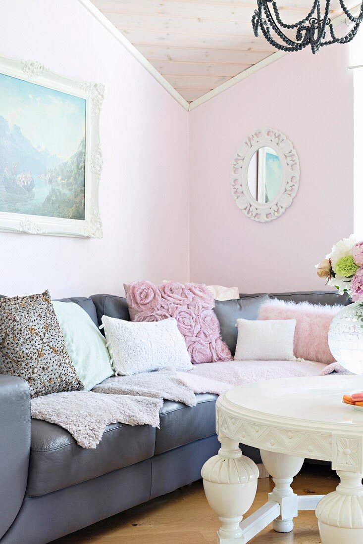 Grey leather couch with various scatter cushions with white coffee table in living room with walls painted pastel pink