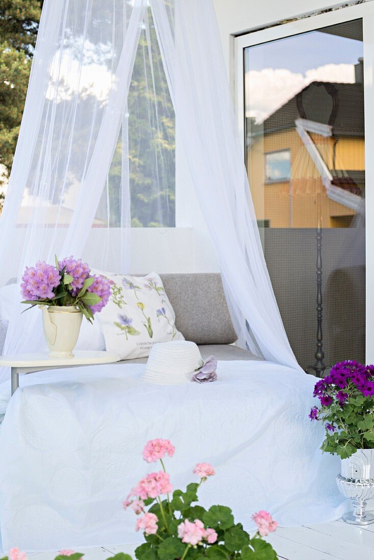 Tagesbett mit Baldachin und Blumen in lila Tönen auf Terrasse