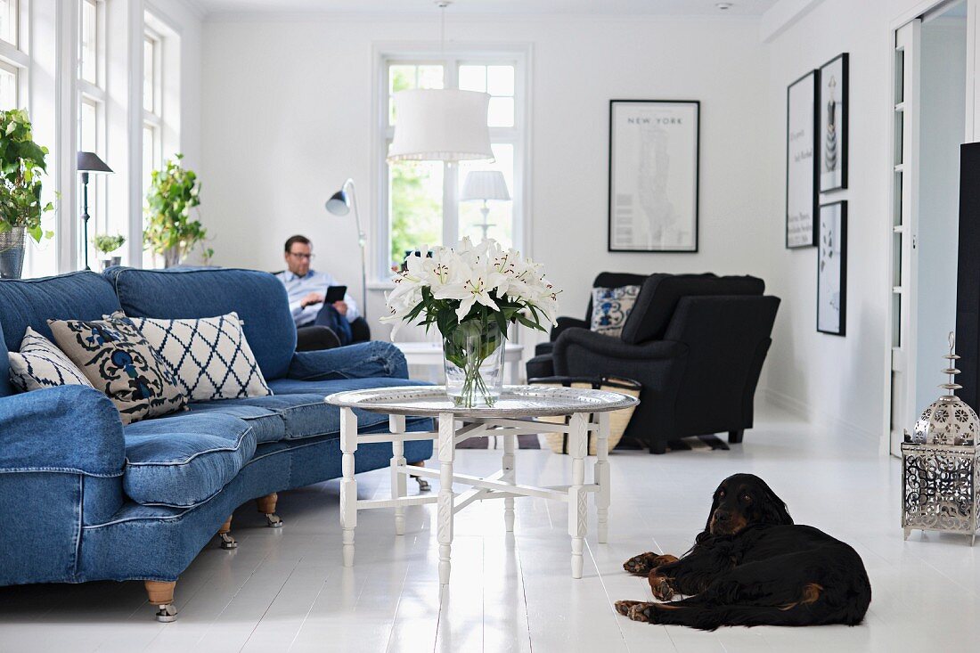 Curved sofa with denim upholstery and tray table in living room; black dog lying on white-tiled floor in foreground