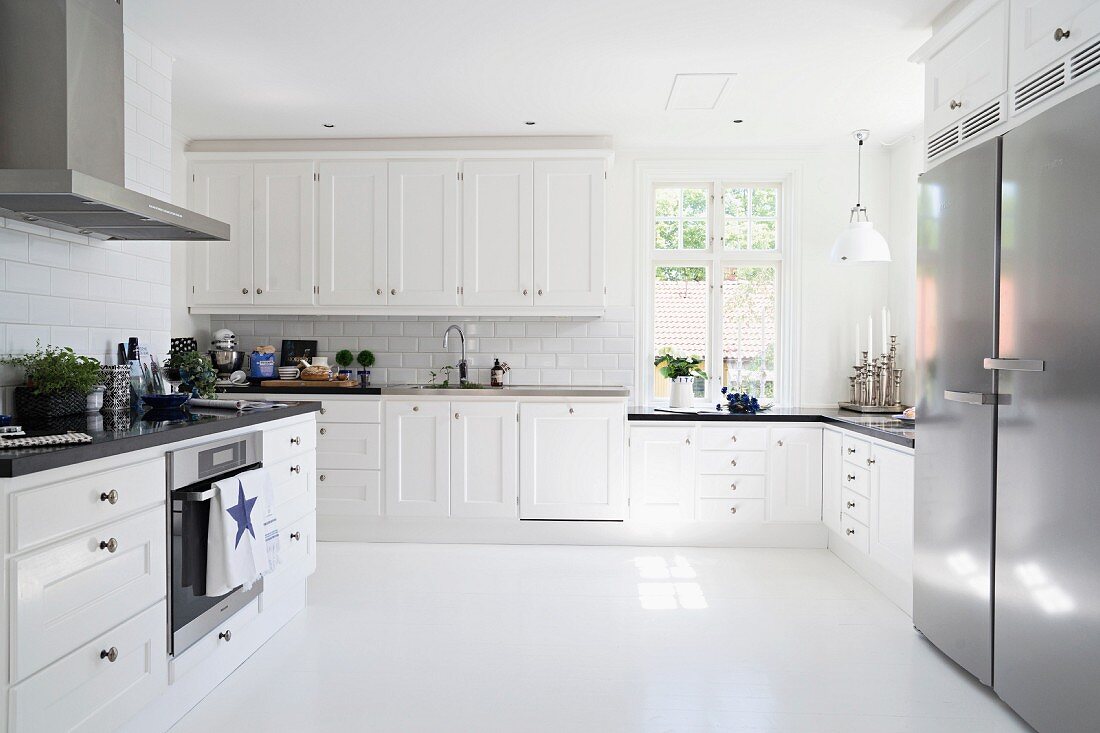 Geräumige, weiße Küche im skandinavischen Stil mit schwarzer Arbeitsplatte und Edelstahlgeräten
