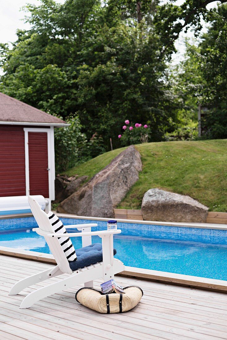 Weisser Stuhl auf Holzterrasse an Pool mit Gartenblick