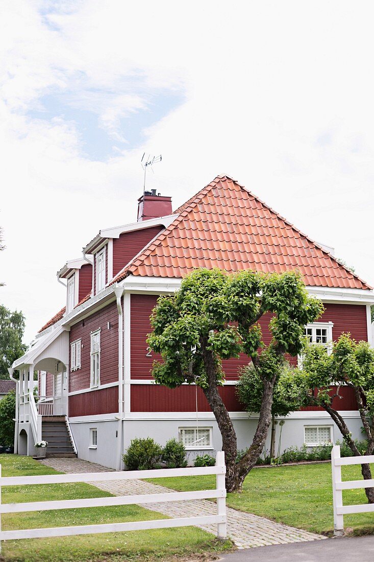 Front garden of traditional Swedish house with wooden elements painted Falu red and white