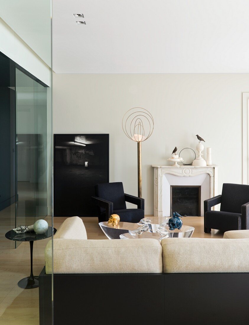 Blick über Sofa auf elegante dunkle Sessel und Stehleuchte aus Messing in minimalistischem Wohnzimmer