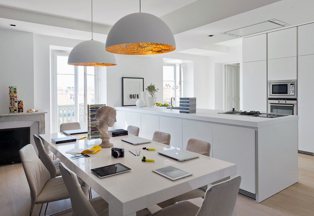 Offene, helle Küche mit modernem Tisch unter Hängeleuchten mit weißem und goldfarbenem Lampenschirm