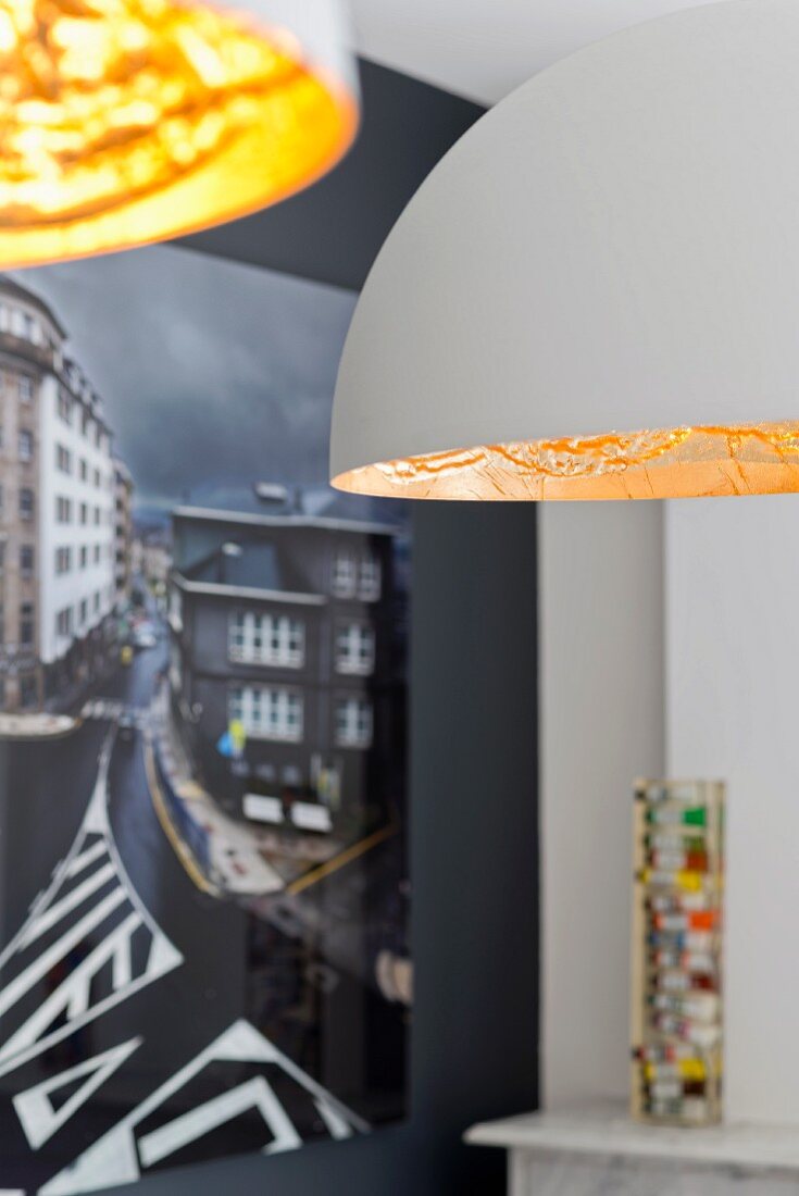 Detail of two pendant lamps with white and gold lampshades; photographic art on black wall in background