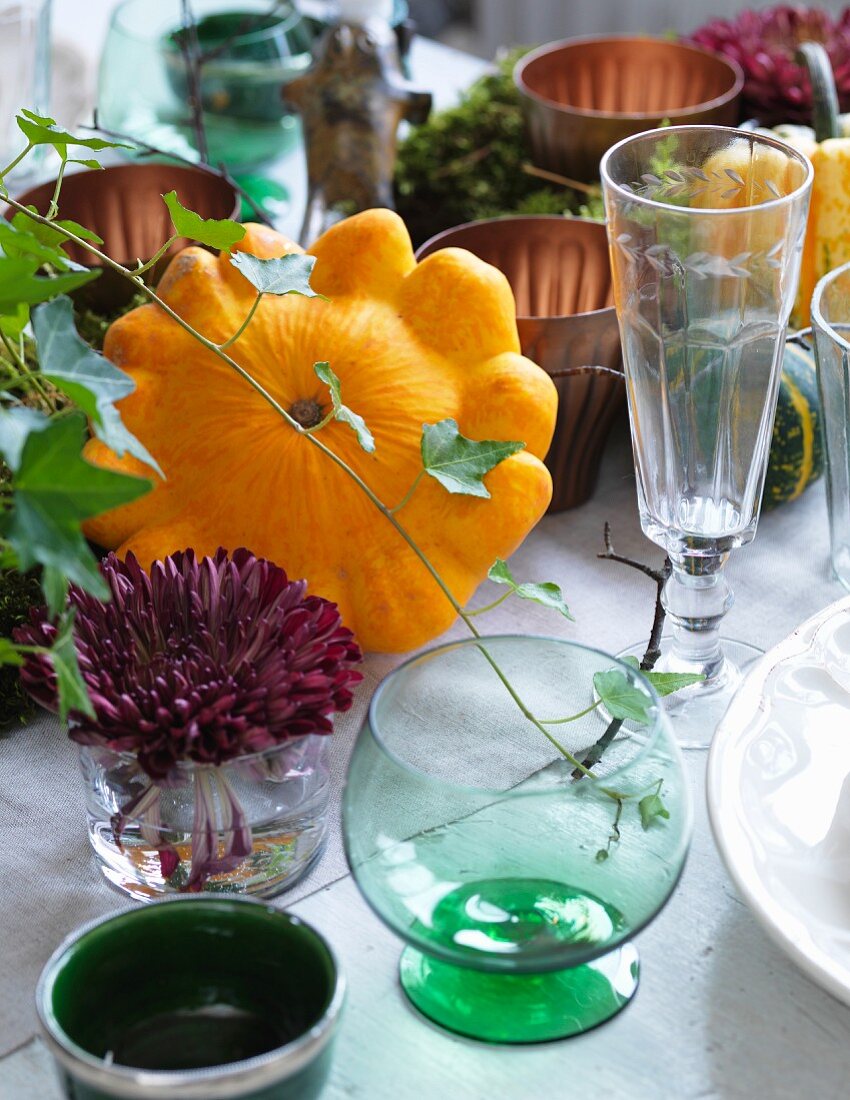 Autumnal arrangement of pattypan squash, ivy, moss and drinking glasses on table