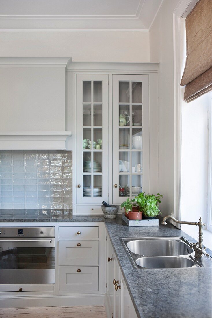 Corner of kitchen with country-house-style, glass-fronted cabinets and sink with vintage tap fittings