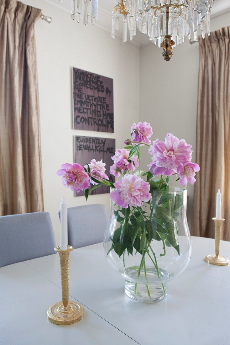 Blumenstrauss mit pinkfarbenen Pfingstrosen zwischen Kerzenhaltern auf Tisch