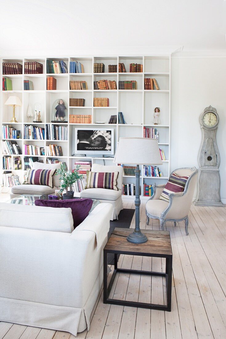 Holz Beistelltisch mit Tischleuchte neben Sofa, im Hintergrund Sesseln vor eingebautem Bücherregal