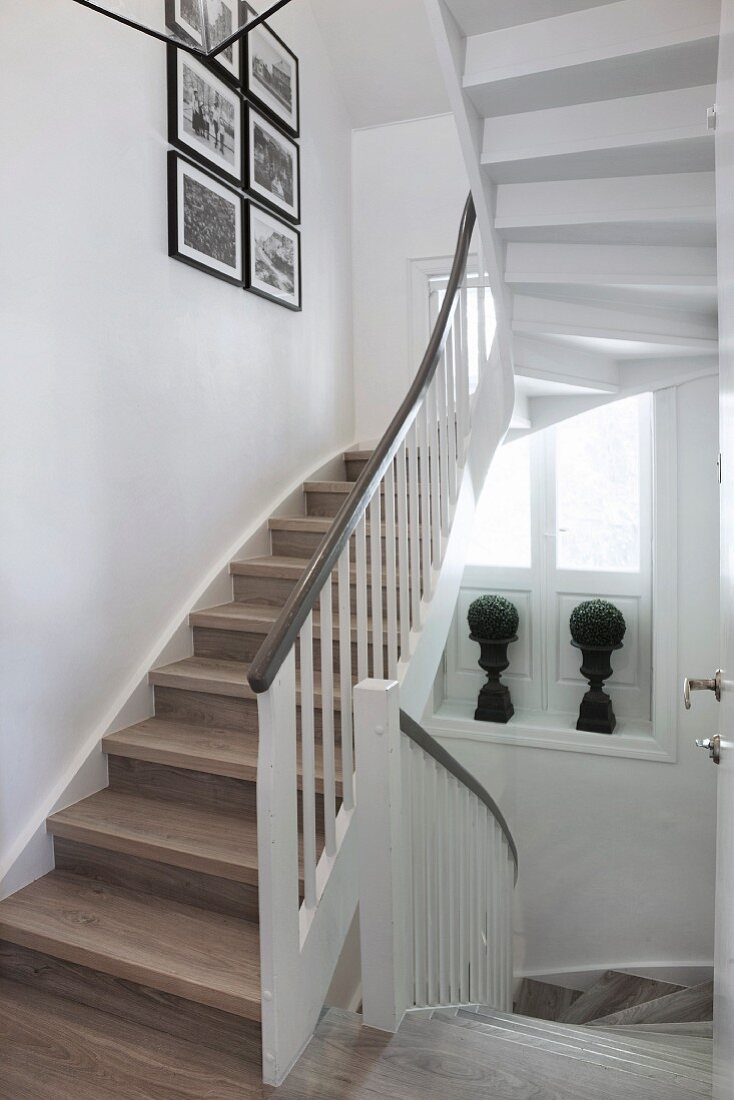 Ländliches Treppenhaus mit gewendelter Treppe und weisses Geländer, an Wand Bilder