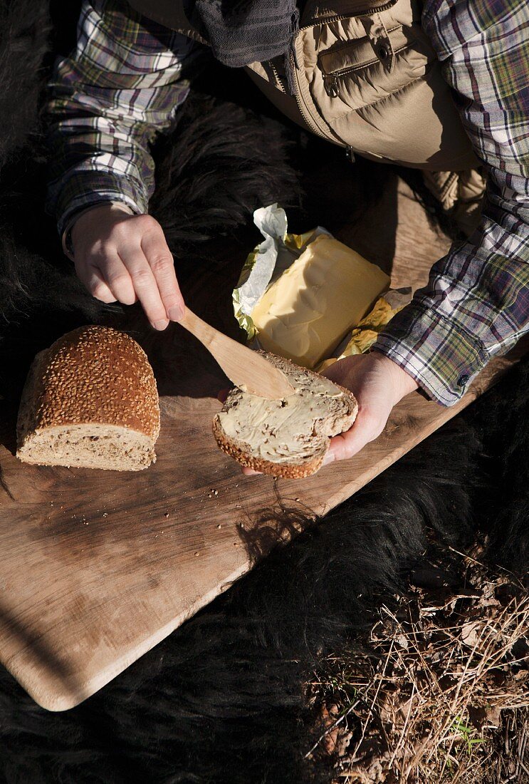 Woman's hands holding bread and butter outdoors with wooden board and fur blanket