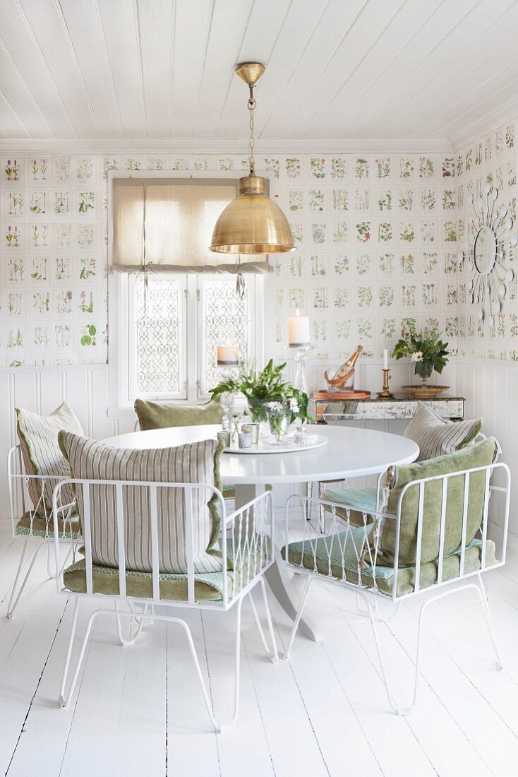 weiße Metallstühle mit Kissen um rundem Tisch in Esszimmer mit botanischem Tapetenmuster und weißem Dielenboden