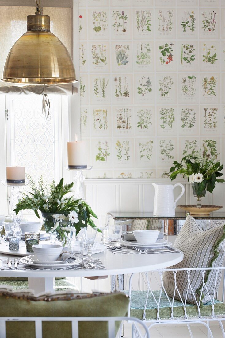 Gedeckter Tisch mit weißem Geschirr und Blumenstrauss in Esszimmer, an Wand Tapete mit botanischem Muster