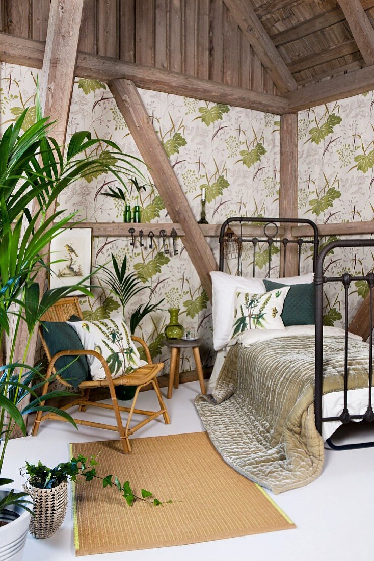Black, retro, metal grille bed and bamboo chair in rustic, half-timbered interior with foliage plants and leaf-patterned wallpaper