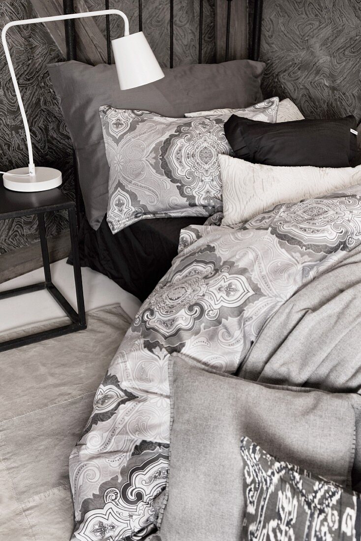 weiße Retro Nachttischleuchte auf Beistelltisch neben Bett, mit grau gemusterter Bettwäsche